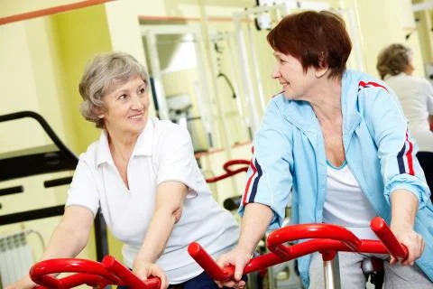 Portrait of two active seniors sitting on exercise bicycles Stock Photos