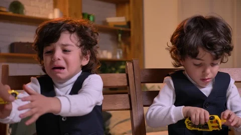 Portrait of two arabic curly-headed twins sitting on chairs in living room Stock Footage 99757392