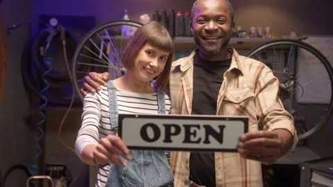 Portrait of two attractive cheerful workers of bike shop workshop holding open Stock Footage 232868653