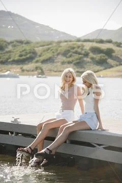 Portrait of two blond sisters sitting on a jetty Stock Photos