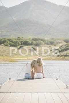 Portrait of two blond sisters sitting on a jetty Stock Photos