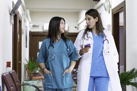 Portrait of two female doctors using mobile phone in corridor at hospital Stock Photos