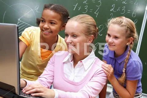 Portrait of two girls and teacher looking at the laptop in classroom Stock Photos