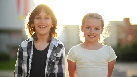 Portrait of Two Happy Kids Smiling Outdoors. The Rays of the Sun Shine On Their Stock Footage
