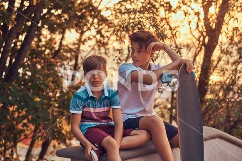 Portrait of two little brothers with a skateboard sitting on the stone guardrail Stock Photos