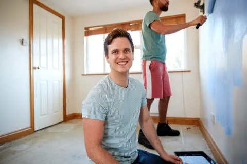 Portrait Of Two Men Decorating Room In New Home Painting Wall Together 스톡 사진