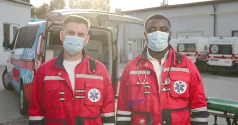 Portrait of two mixed-races young males paramedics in uniforms and masks Video stock 158316414