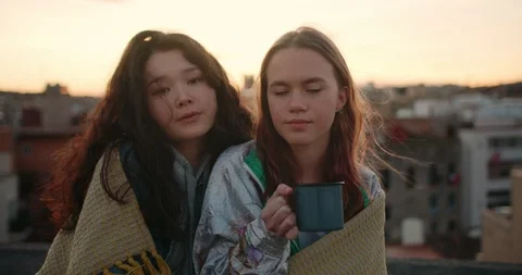 Portrait of two pensive pleasant mixed race teen girls wrapped in plaid at Stock Footage 125309963