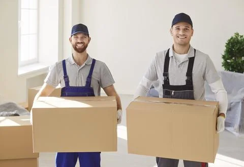 Portrait of two smiling movers in uniform holding cardboard boxes, assisting in Stock Photos