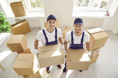 Portrait of two smiling professional movers effortlessly carrying cardboard Stock Photos