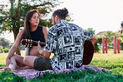 Portrait of two young and future parents in a park on a blanket and him playi Stock Photos