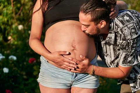 Portrait of two young future parents outdoors, while he kisses his wife's bel Stock Photos
