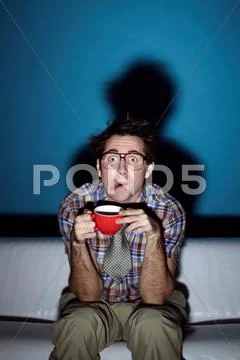 Portrait of typical nerd watching TV with cup of coffee in hands Stock Photos