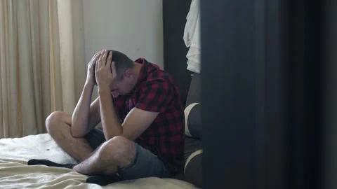 Portrait of upset millennial young man sitting on a bed. Frustrated sad man thin Stock-Footage 249401508