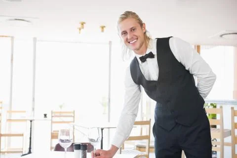 Portrait of waiter standing at table with empty glass in restaurant Foto stock