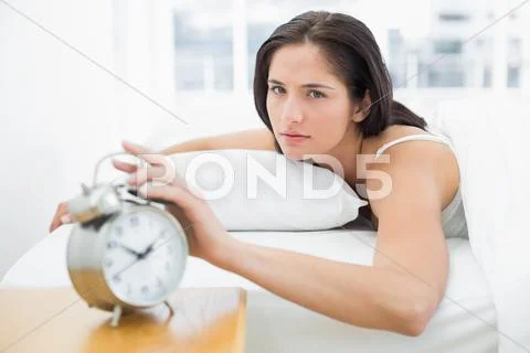 Portrait of a woman in bed extending hand to alarm clock Stock Photos