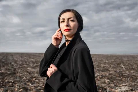 Portrait of a woman in a black coat whose hair is flying in the wind stands in a Stock Photos