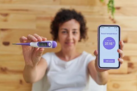 Portrait of a woman looking at camera while taking her basal temperature Foto stock