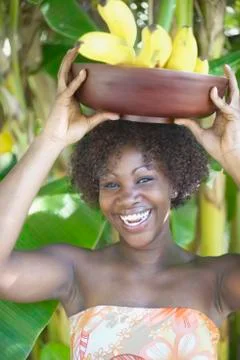 Portrait of woman smiling with bowl of bananas balanced on head Stock Photos