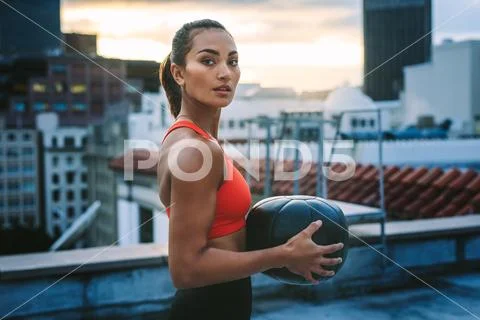 Portrait of a woman standing on rooftop holding a medicine ball Stock Photos