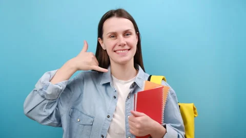 Portrait of woman student with backpack doing phone gesture says call me back Stock Footage 264164245