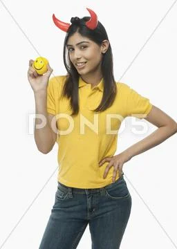 Portrait of a woman wearing devil's horns and holding a smiley face ball Stock Photos