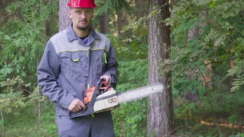 Portrait of worker in a helmet with a chainsaw in the forest. The man looks Stock Footage 113391029