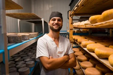 Portrait of young artisan cheese maker smiling between rows of ageing cured Stock Photos