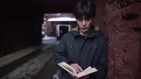 Portrait of young Asian student reading book outdoors on old city street Stock Footage