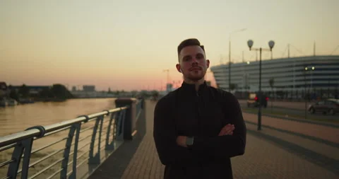 Portrait of young athletic man smiling at camera on a city pier at sunset Stock Footage 276542894