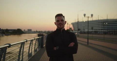 Portrait of young athletic man smiling at camera on a city pier at sunset Stock Footage 276542959