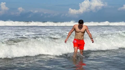 Portrait of young athletic smiling man with bare torso emerging from ocean  Video stock 183458444