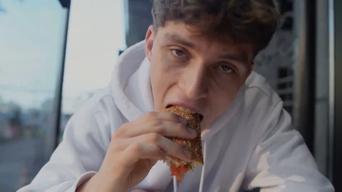 Portrait of young attractive smilling guy eating sandwich and thinking in fast Video stock 101014732