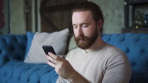 Portrait of young bearded guy is using smartphone and having good time at Stock Footage 134873083
