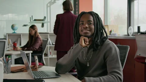 Portrait of Young Black Man Smiling at Camera while Sitting at Office Desk Video stock 333394814