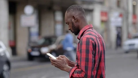 Portrait of young black man typing on smartphone in the street Stock Footage 87337613