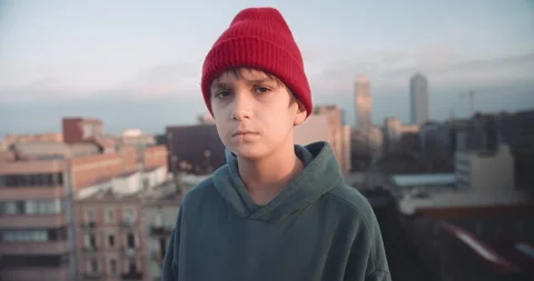 Portrait young boy on rooftop at sunset wearing hoody and beanie red hat looking Stock-Footage 139595452