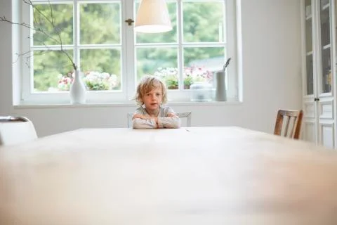 Portrait of young boy sitting at empty dining table Stock Photos