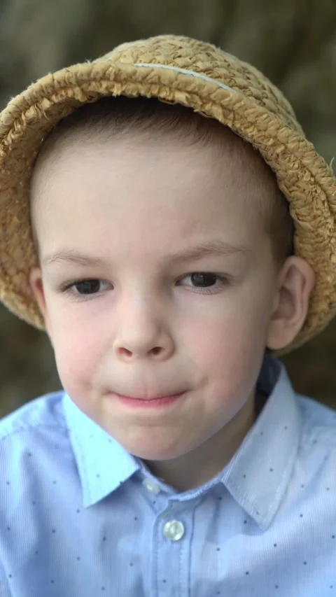 Portrait of a young boy in a straw hat biting his lips and looking at the camera Stock Footage 347101838