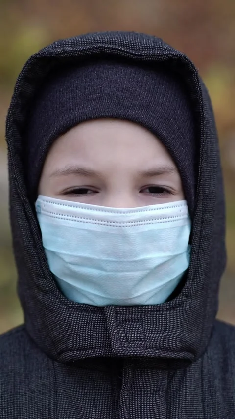 Portrait of a young boy wearing a dark hoodie and blue surgical mask Stock Footage 344891047