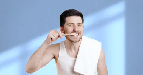 Portrait of a young brunette with a beard brushing his teeth in the bathroom on Stock Footage 234782473