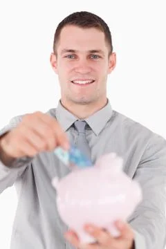 Portrait of a young businessman putting a twenty euros note in a piggy bank Stock Photos