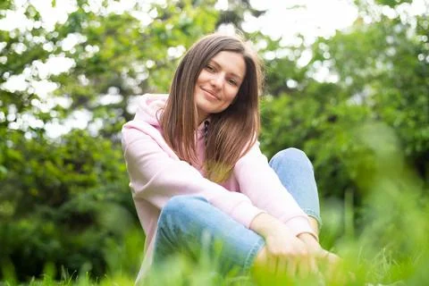 Portrait of a young cheerful woman sitting in the park on the green grass in a p Stock Photos