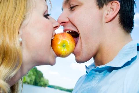 Portrait of a young couple biting on an apple between their mouths Stock Photos