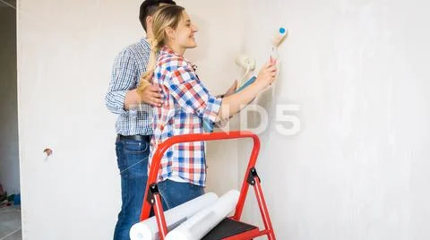 Portrait of young couple painting walls in new house with white paint Stock Photos