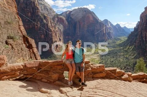 PORTRAIT: Young couple sitting on rocky ledge and posing in front of epic valley Stock Photos