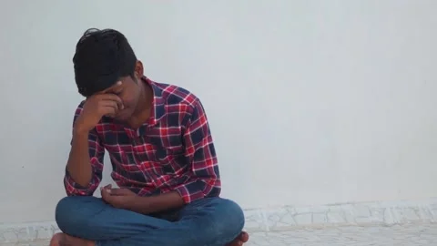 Portrait of a young depressed Indian kid holding his head while sitting alone.  Stock Footage