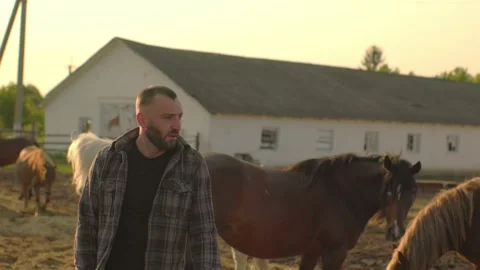 Portrait of a young farm worker, on the background of a fence with horses. Video stock 251111241