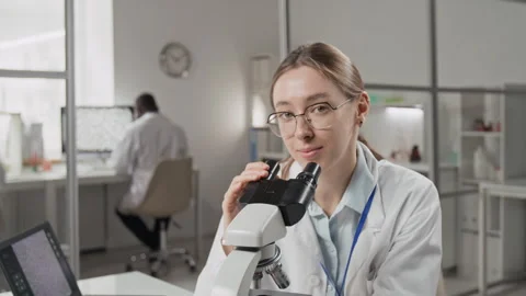 Portrait of Young Female Scientist Using Microscope, Sitting at Desk in Lab Stock Footage 321899775