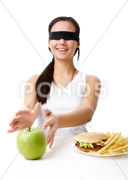 Portrait of young girl with her eyes folded deciding what to eat: an apple or fa Stock Photos